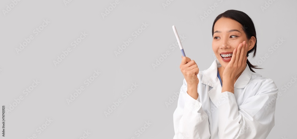 Happy Asian doctor with pregnancy test on grey background with space for text Happy Asian doctor with pregnancy test on grey background with space for text