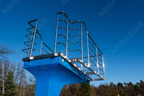 Obraz na płótnie A blue diving board over an empty swimming pool. Stainless steel rails around the platform. The outdoor swimming pool is ready for the seasonal break. w salonie