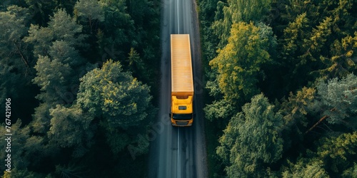 Aerial view of yellow heavy truck on a narrow twisting road through forest area.