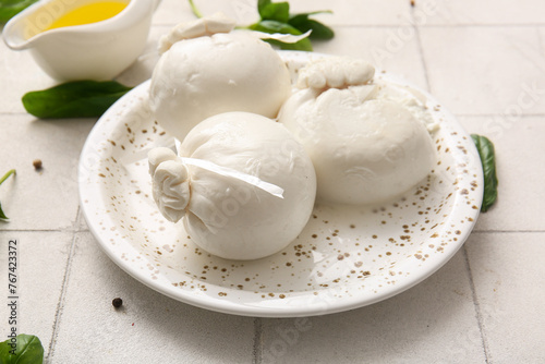 Plate of tasty Burrata cheese with basil on white tile background