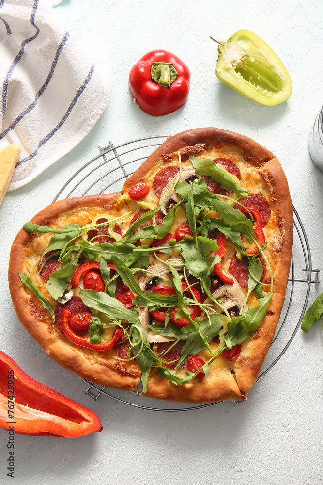 Stand with tasty heart shaped pizza and pepper on light blue background