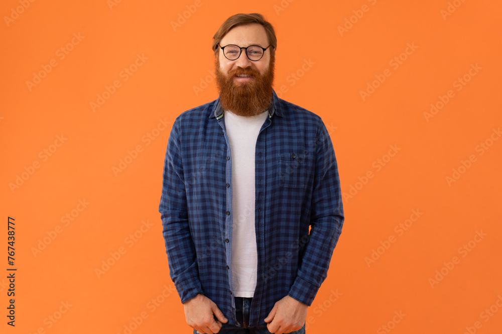 Fototapeta premium Smiling redhaired man with beard wearing glasses on orange background