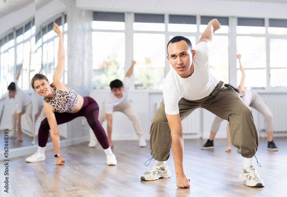 Group of young people, girls and guys in sportive casual style clothes dancing in choreography class