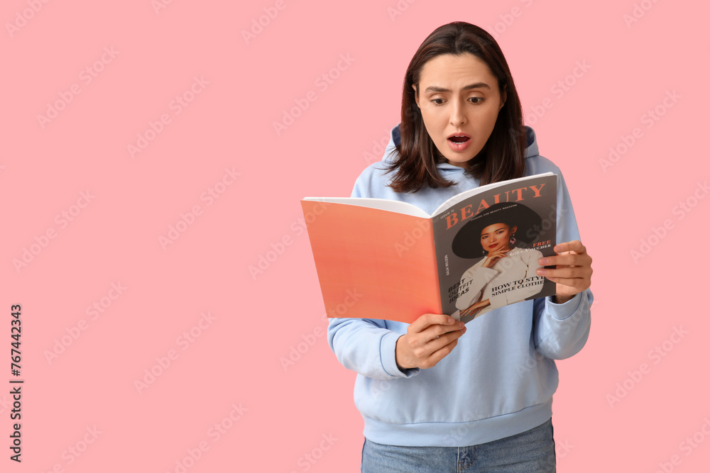 Fototapeta premium Shocked young woman reading beauty magazine on pink background