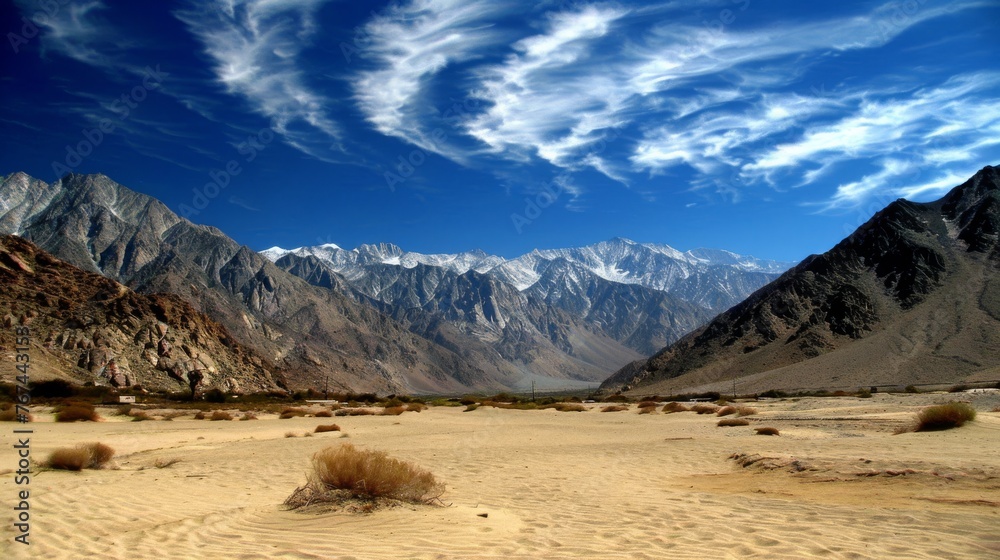  a desert area with mountains in the background and a blue sky with wispy clouds in the foreground.