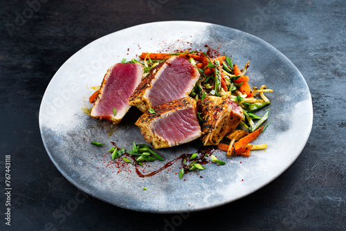 Traditional Japanese gourmet tuna fish steak tataki with vegetable slices and soy sprouts with sweet dour sauce served as close-up on a Nordic design plate with copy space photo