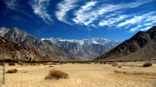  a desert area with mountains in the background and a blue sky with wispy clouds in the foreground.