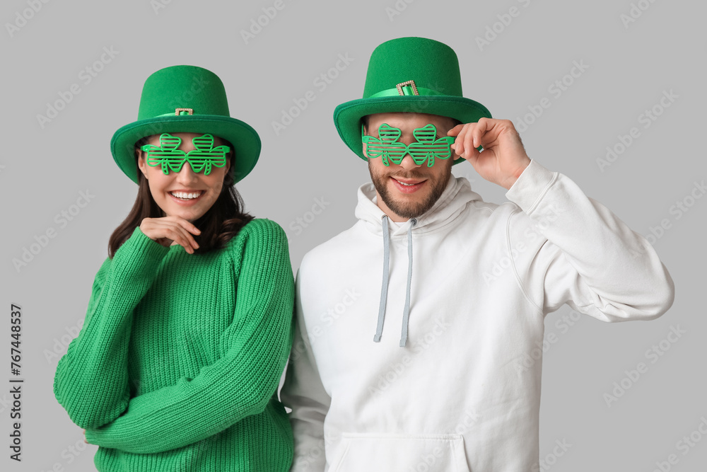 Beautiful young couple in leprechaun hats and decorative glasses in shape of clover on grey background. St. Patrick's Day celebration Beautiful young couple in leprechaun hats and decorative glasses in shape of clover on grey background. St. Patrick's Day celebration