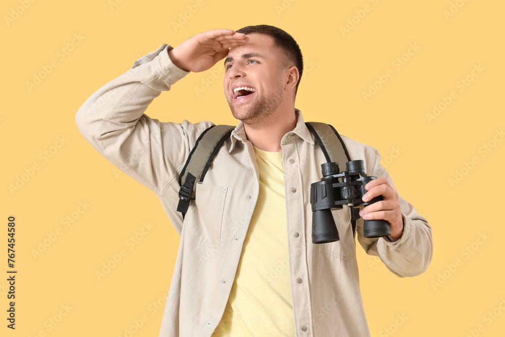 Male tourist with backpack and binoculars on yellow background Male tourist with backpack and binoculars on yellow background