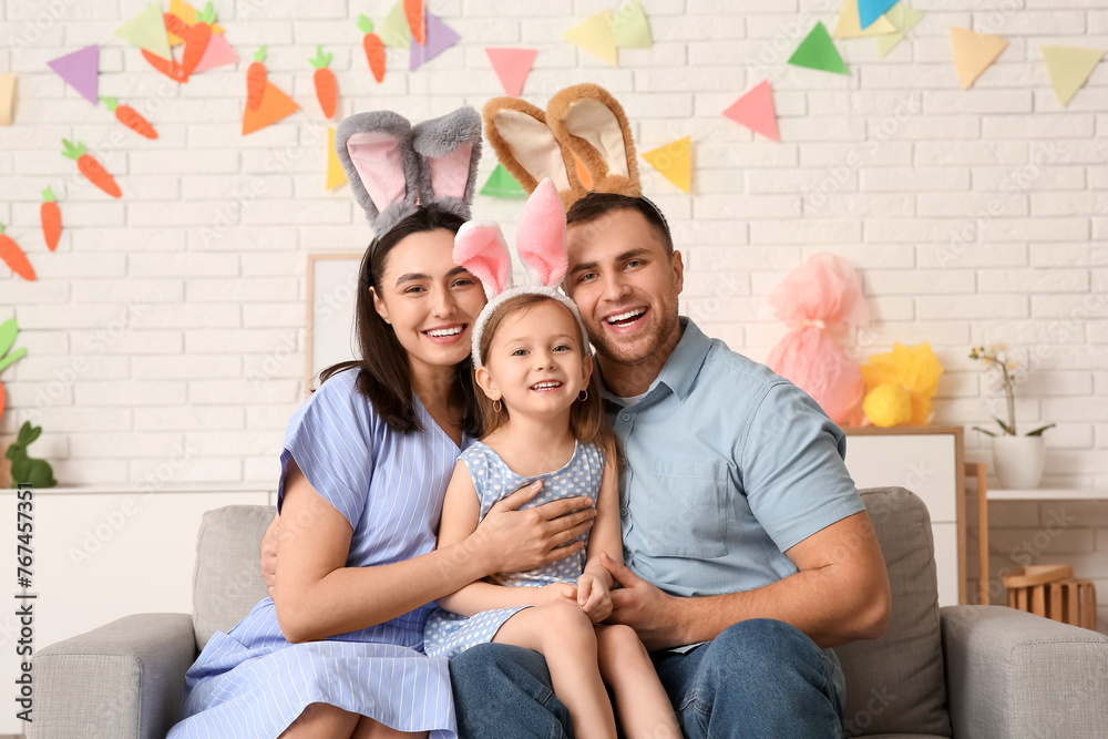 Happy family in Easter bunny ears sitting on sofa at home - obrazy, fototapety, plakaty 