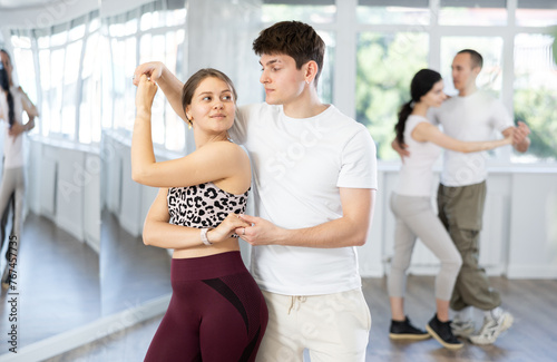 Happy young woman in sportswear with man dancing bachata in modern ballroom dance class