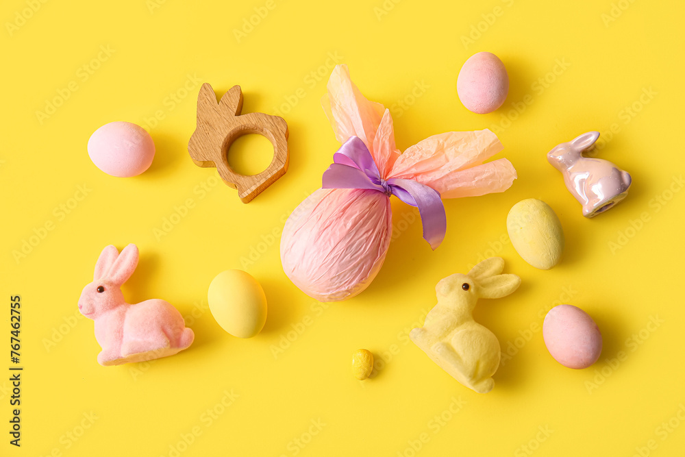 Painted and chocolate Easter eggs wrapped in paper with toy bunnies on yellow background