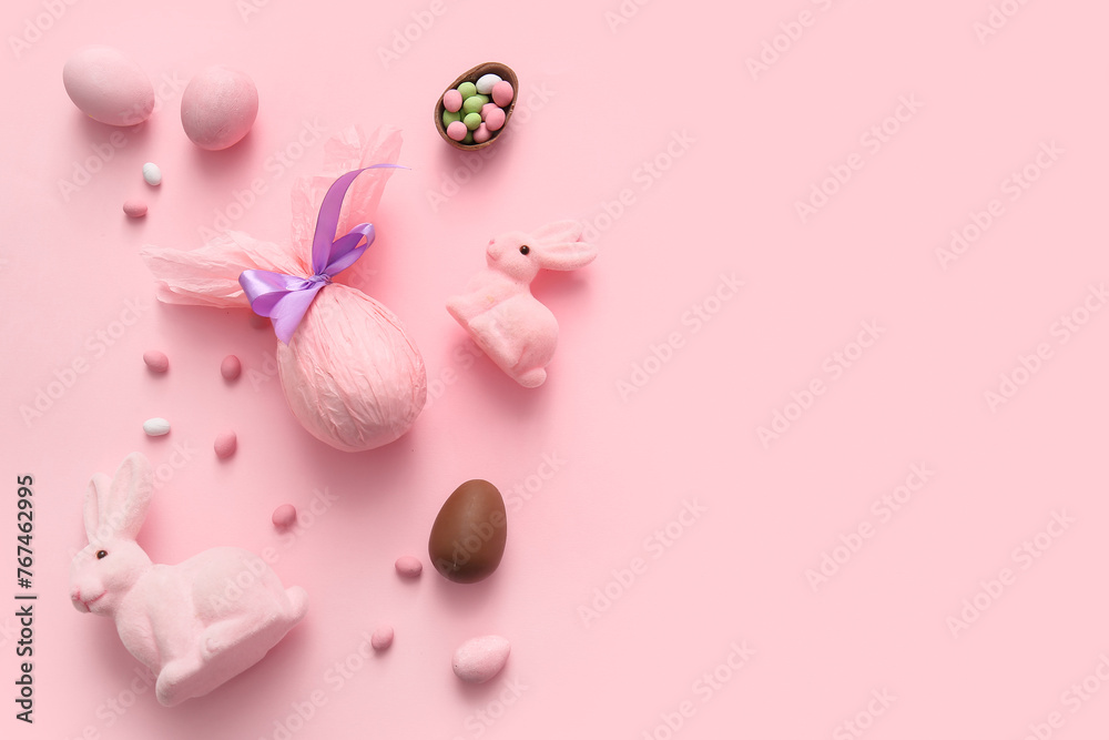 Painted and chocolate Easter eggs wrapped in paper with toy bunnies on pink background
