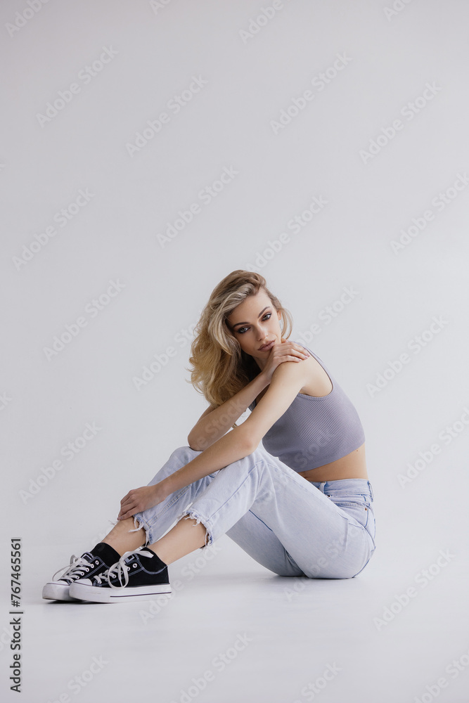 Fototapeta premium Full-length portrait of an attractive young girl in casual clothes, jeans, sneakers and a gray top.