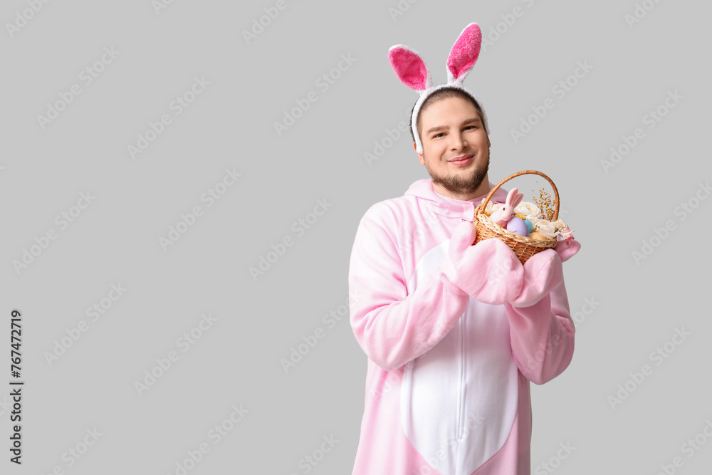 Young man in bunny costume with Easter basket on grey background Young man in bunny costume with Easter basket on grey background