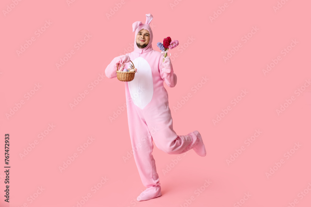 Young man in bunny costume with Easter basket and beautiful flowers on pink background Young man in bunny costume with Easter basket and beautiful flowers on pink background