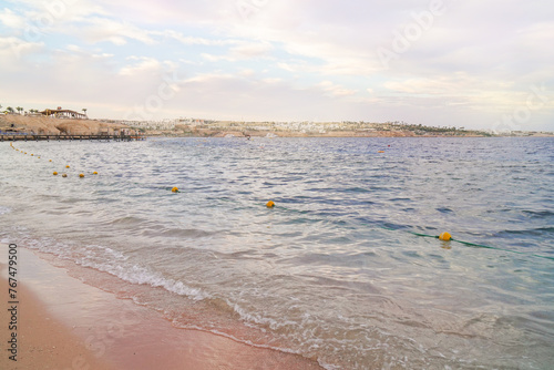 Scenic seaside view with calm waves, beach, and a coastal cityscape in the background.