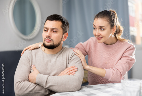 Canvas Print Tender loving young woman comforting distressed offended husband after spat while sitting together at table at home