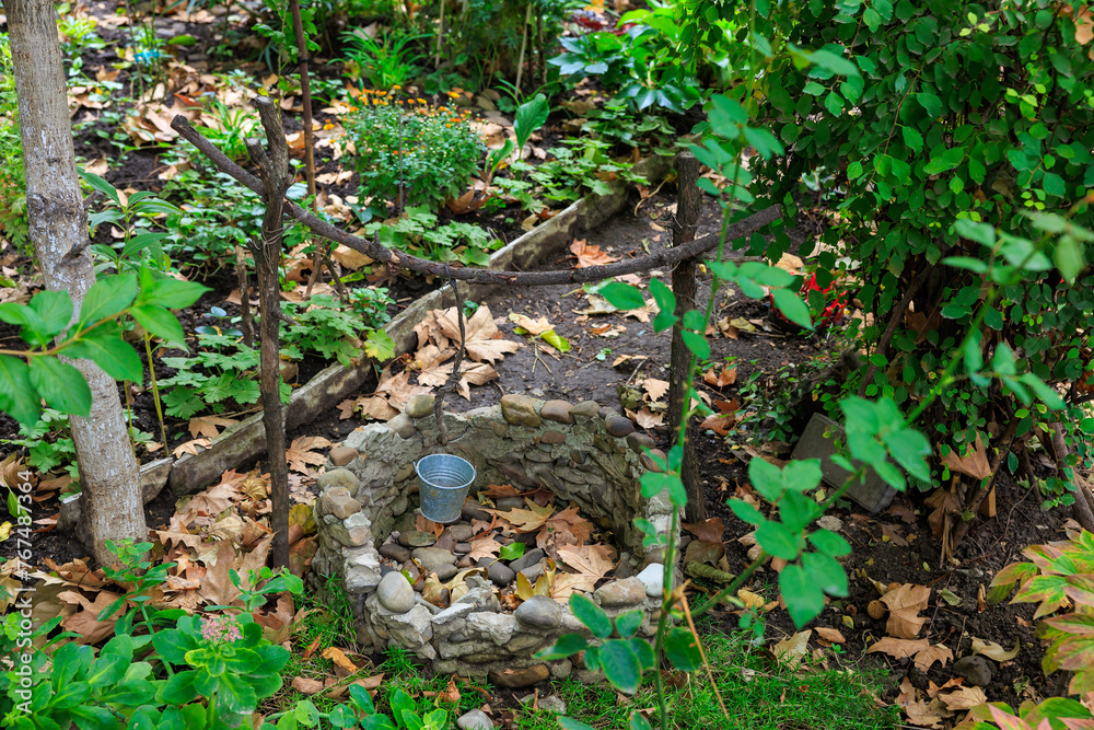 A small garden with a stone basin and a metal bucket A small garden with a stone basin and a metal bucket