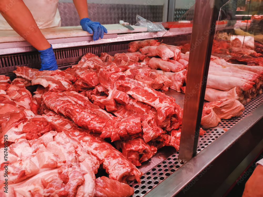 Nutritious raw meat of pork ribs along with pig elbows and legs, shopping at local butcher shop,Butcher wears blue gloves for hygiene