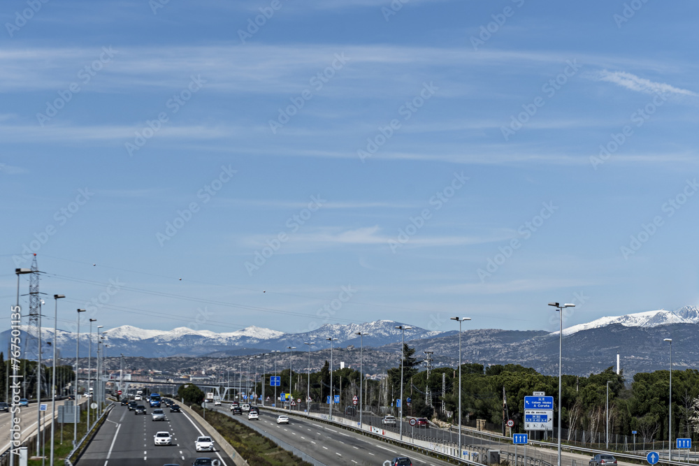 a highway next to a forest in the direction of the snowy mountain of the Sierra de Navacerrada
