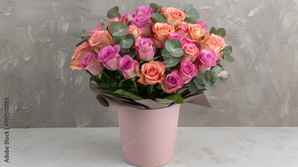  a bouquet of pink and orange roses in a pink vase on a white table with a gray wall in the background.