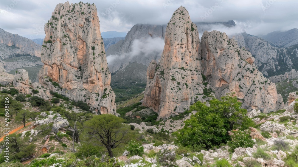  a group of rocks in the middle of a mountain range with trees in the foreground and clouds in the background.