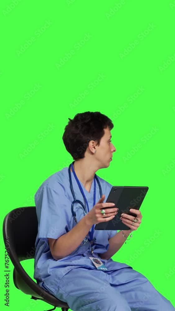 Side view Medical assistant browsing internet on tablet while she sits down in a chair, killing time by scrolling on social media apps and texting friends. Nurse in scrubs using modern gadget. Camera Side view Medical assistant browsing internet on tablet while she sits down in a chair, killing time by scrolling on social media apps and texting friends. Nurse in scrubs using modern gadget. Camera