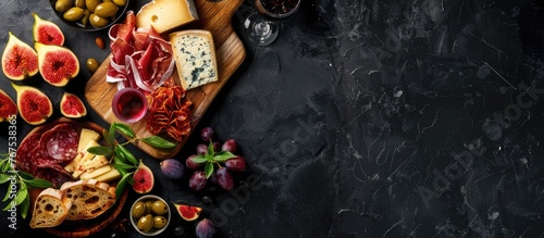 A variety of cheeses, figs, bread, olives, and prosciutto displayed with a red wine selection on a wooden board against a black background, with empty space for text, top-down view. photo