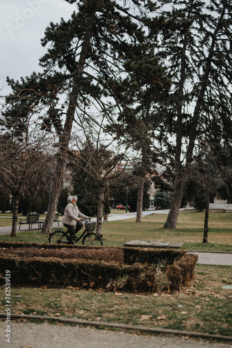 An elderly lady on a bicycle takes a leisurely ride through a serene, tree-lined park amidst the tranquility of nature.