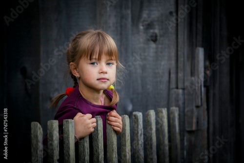 A cute little girl looks out from behind a rustic wooden fence.