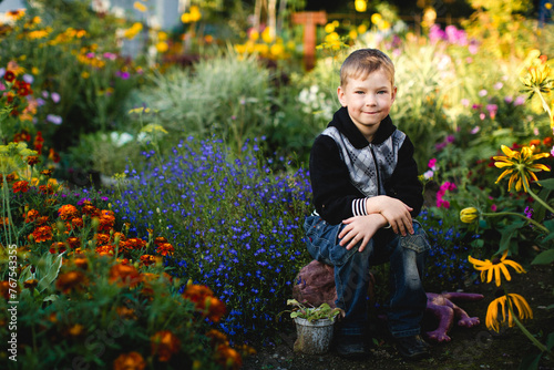 A boy sits in a garden with flowers.