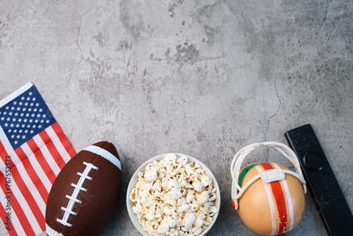 Top view of popcorn, American flag, rugby ball and remote control over grey background with copy space. Super bowl concept. photo
