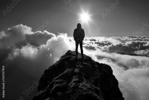 Silhouette of a person standing on a mountain peak looking down on the clouds under the sun rays, monochrome outdoors adventure © John