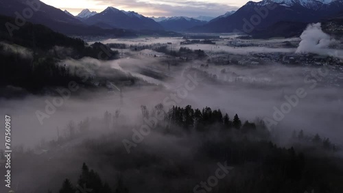 Aerial Drone shot over misty Cityscape at Sunrise Surrounded by Snow Covered Mountains in Frastanz, Vorarlberg, Austria photo