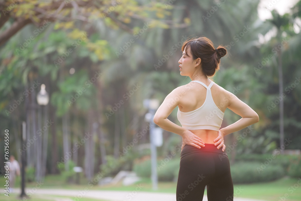 Back pain problem. woman jogger. 30s asian female wearing white sportswear holding her back with pain after running exercise in public park. Back pain problem. woman jogger. 30s asian female wearing white sportswear holding her back with pain after running exercise in public park.
