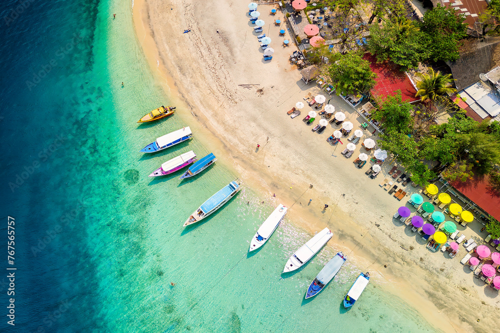 Top down view of colorful sunshades and tourist boats on a tropical beach