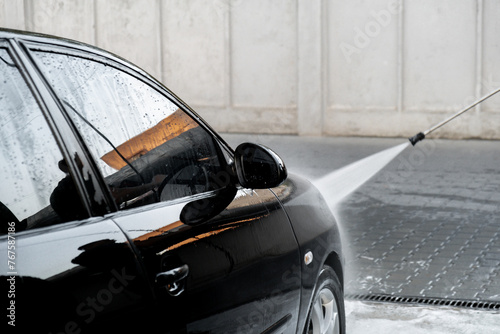 Washing luxury black car on touchless car wash. Cleaning the details of car. Washing sedan car with foam self-service and high pressure water. Cleanliness and order in urban environment photo