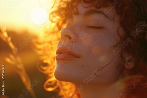 A woman with red hair and freckles is looking at the camera with a peaceful expression. The sun is shining brightly, casting a warm glow on her face. Concept of calm and relaxation