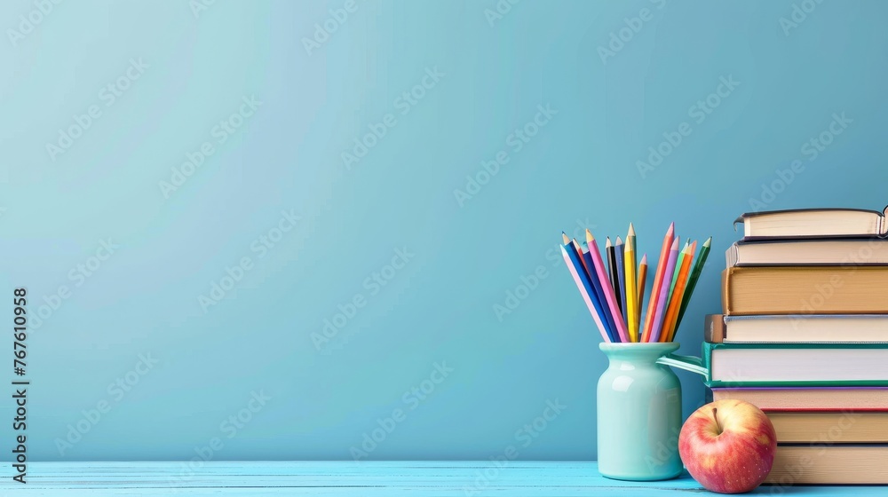 Books and apple next to colorful pencils in vase