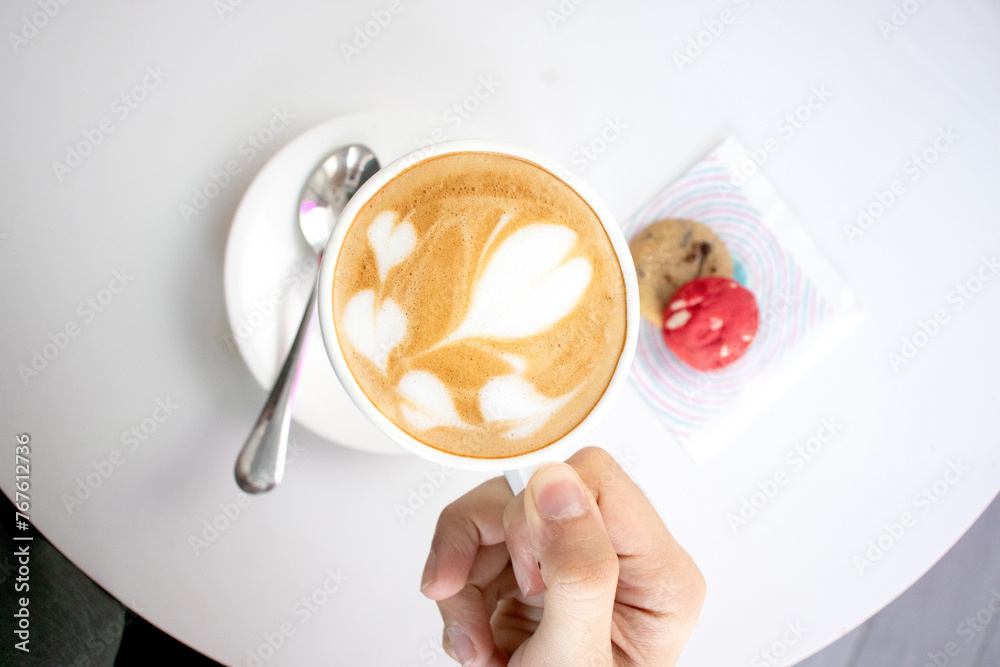 Cappuccino in white cup on a white table with two mini cookies chocolate chip and red velvet. Cappuccino in white cup on a white table with two mini cookies chocolate chip and red velvet.