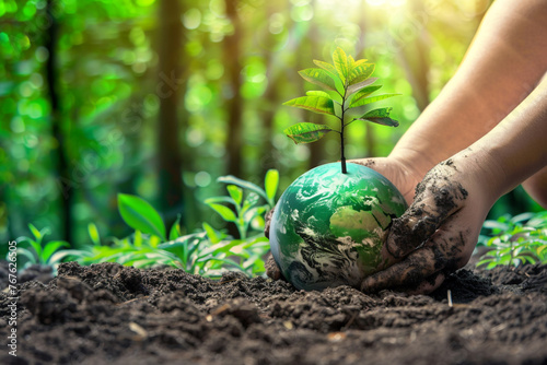 A pair of hands, covered in soil, planting a young tree into a green, vibrant globe, symbolizing the act of nurturing the planet photo