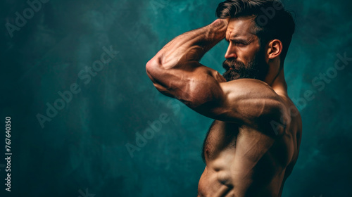 A handsome brutal athlete demonstrates strength and muscles on his arms against an isolated dark background.