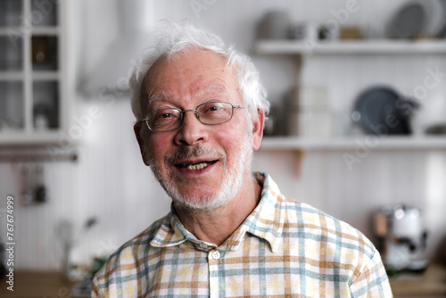 portrait of elderly cheerful man standing in cozy kitchen and smiling photo