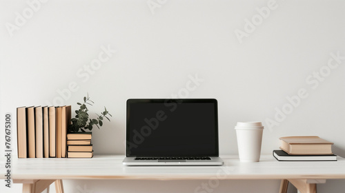 neat workspace with a laptop at the center of a white wooden desk. To the right, there’s a coffee cup, and on the left, a stack of books is neatly arranged. The desk is set against a plain white wall © AdamDiezel