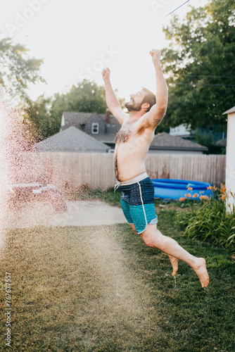 Smiling man jumps through spraying hose water outside during Summer photo