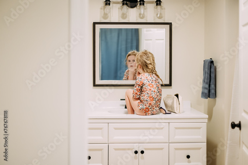Young girl sitting on bathroom counter putting on mom's makeup photo