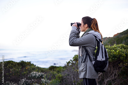 Woman, mountain and binoculars in nature environment for trekking hike for holiday, explore or journey. Female person, workout and walking on wilderness path for healthy, backpacking or adventure