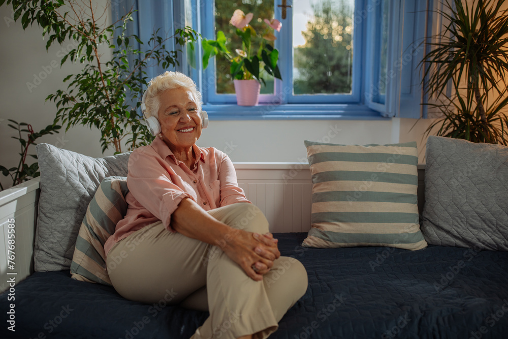 Obraz premium Elderly woman sitting on the sofa and enjoying music