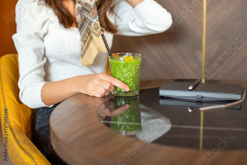 Woman hand holding glass of a green smoothie in the restaurant